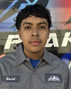 A man wearing a gray work shirt with name tag "Daniel" stands in front of a vehicle with a "PEAK" logo.