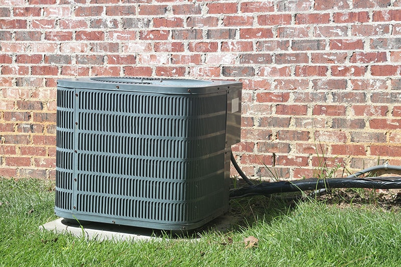 Air conditioning unit outside by brick wall. Tri Peaks Air blog image.