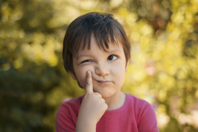 Young kid outside with index finger on face. Wondering when his parents should buy a new air conditioning unit. Tri Peaks Air blog image.