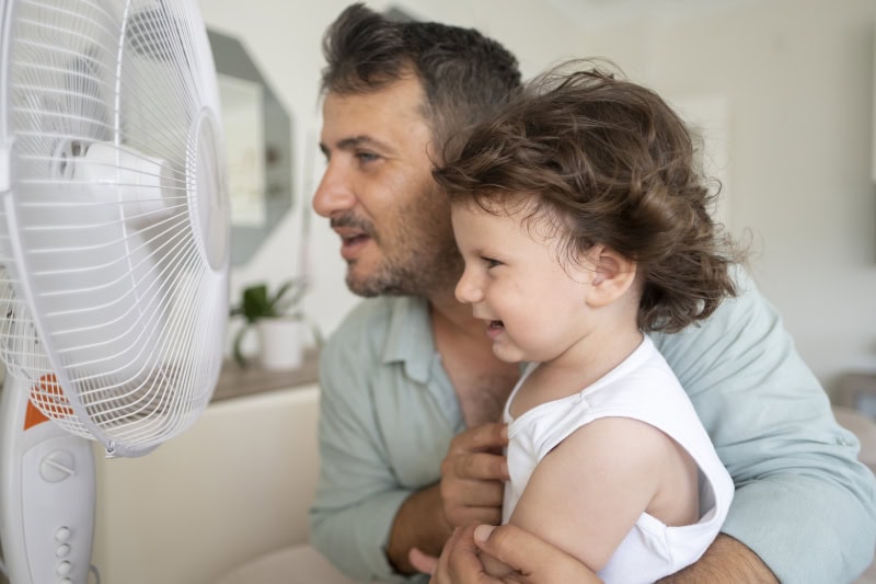 Father and toddler sitting in front of their fan.