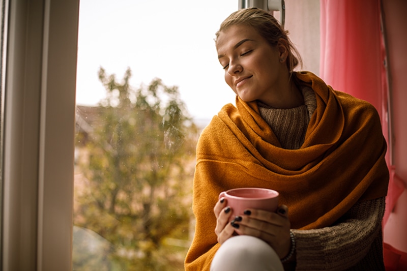 Woman sitting against window with a tree in the background.